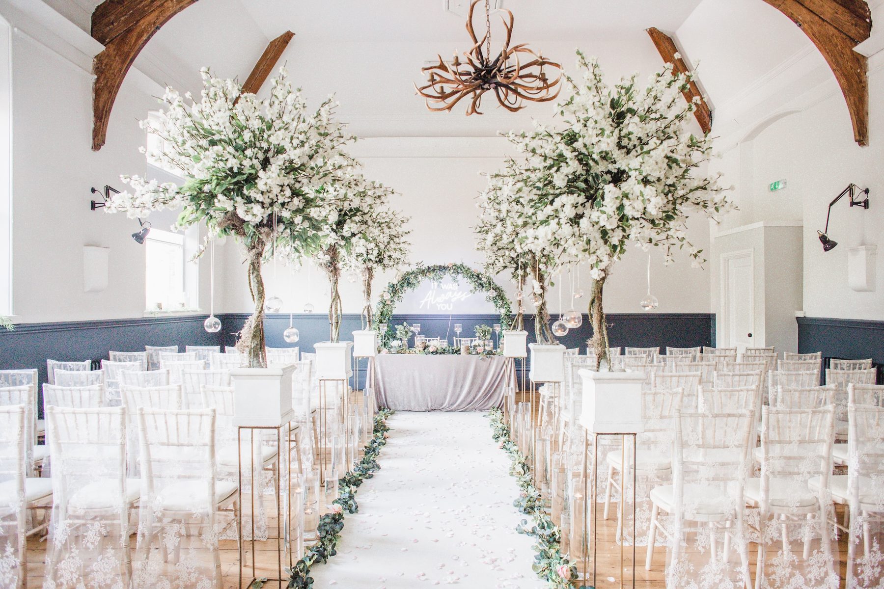 Wedding ceremony aisle in the Ballroom, dressed with blossom trees and a floral arch beneath the original timber ceiling beams