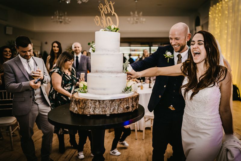 Couple cutting their wedding cake together as guests look on