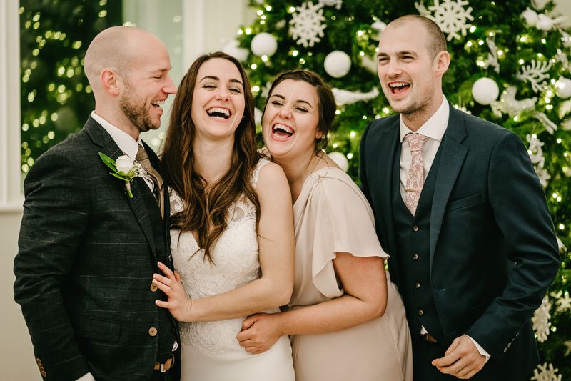 Bride, groom and friends laughing together in front of a decorated Christmas tree