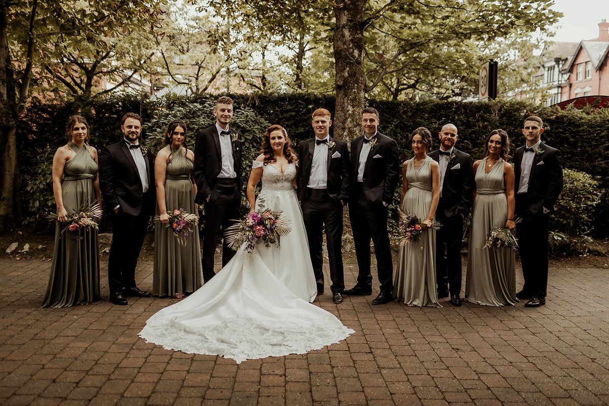 The wedding party in matching olive green dresses and black tuxedos outside Village Point